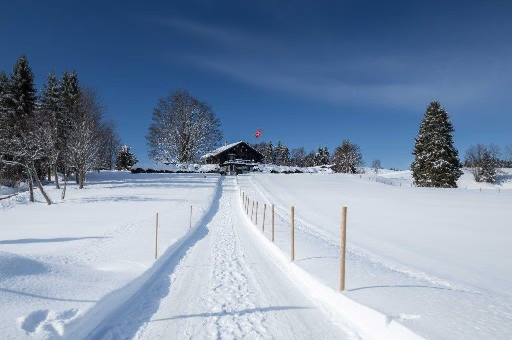 Chemin enneigé vers le chalet Les Ecovets avec drapeau suisse